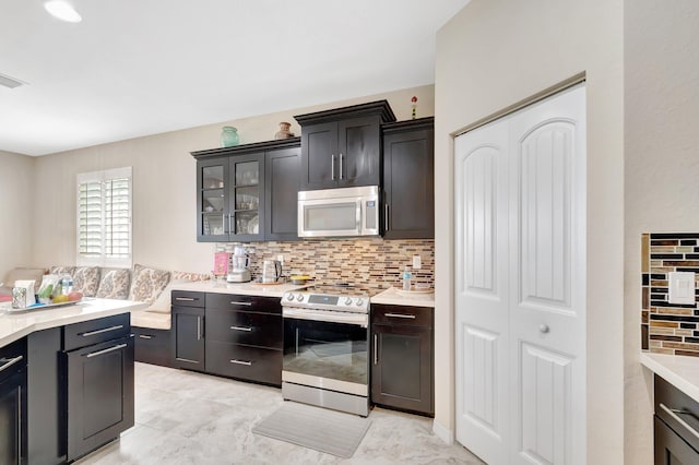 kitchen with light countertops, visible vents, decorative backsplash, appliances with stainless steel finishes, and glass insert cabinets