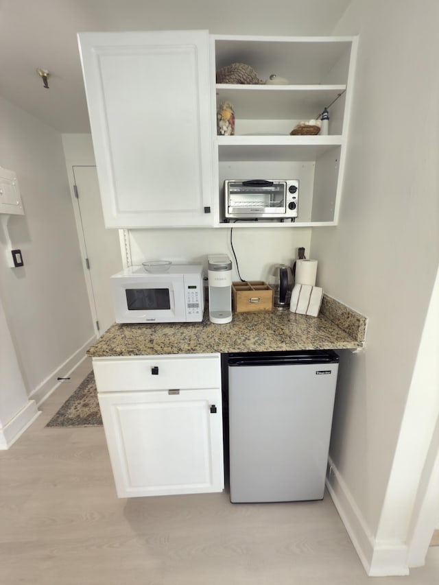 interior space with refrigerator, open shelves, white microwave, white cabinets, and light stone countertops