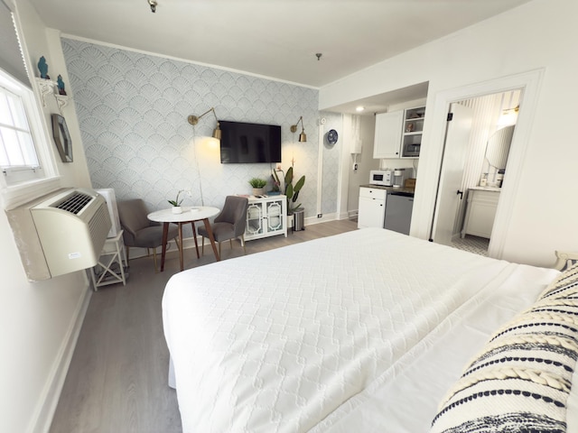 bedroom featuring wallpapered walls, an accent wall, baseboards, and wood finished floors