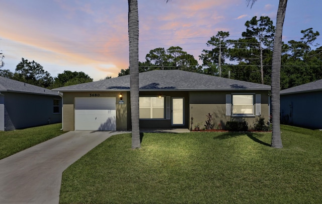 ranch-style home with a garage, a yard, driveway, and stucco siding