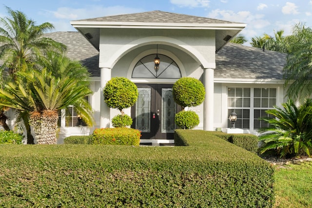 view of exterior entry featuring roof with shingles and stucco siding