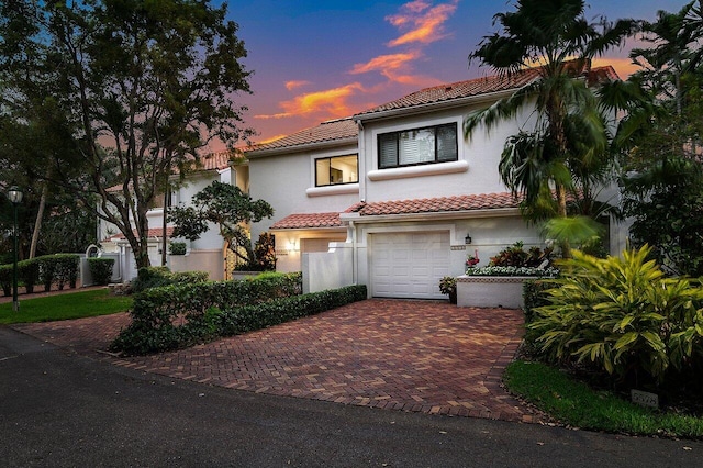 mediterranean / spanish-style home featuring a tiled roof, decorative driveway, an attached garage, and stucco siding