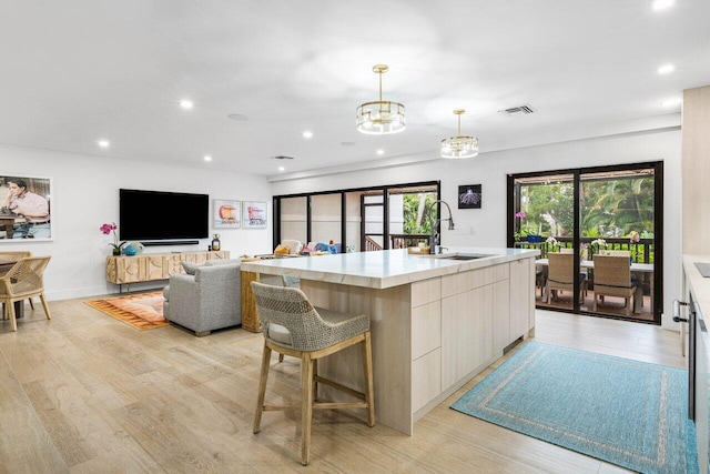 kitchen featuring a kitchen island with sink, a sink, light countertops, hanging light fixtures, and modern cabinets