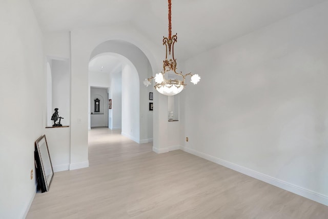 unfurnished room with lofted ceiling, arched walkways, light wood-style flooring, and baseboards