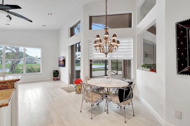 dining area featuring a towering ceiling, light wood-style flooring, baseboards, and ceiling fan with notable chandelier