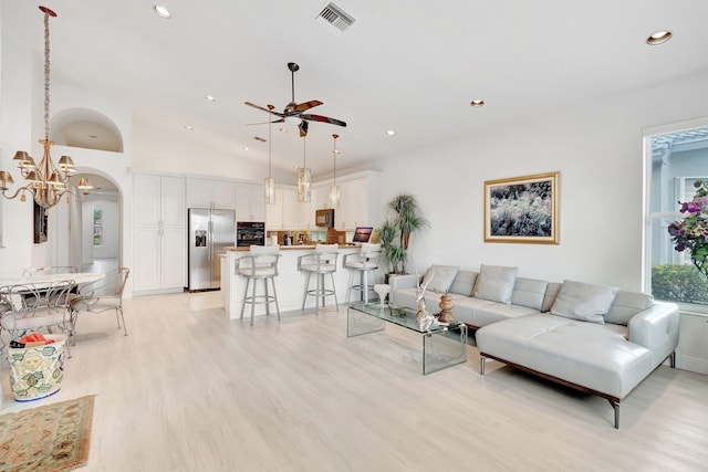 living area with arched walkways, visible vents, light wood-style floors, vaulted ceiling, and ceiling fan