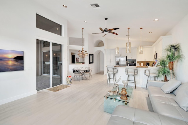 living area with arched walkways, light wood-style flooring, ceiling fan with notable chandelier, a towering ceiling, and visible vents