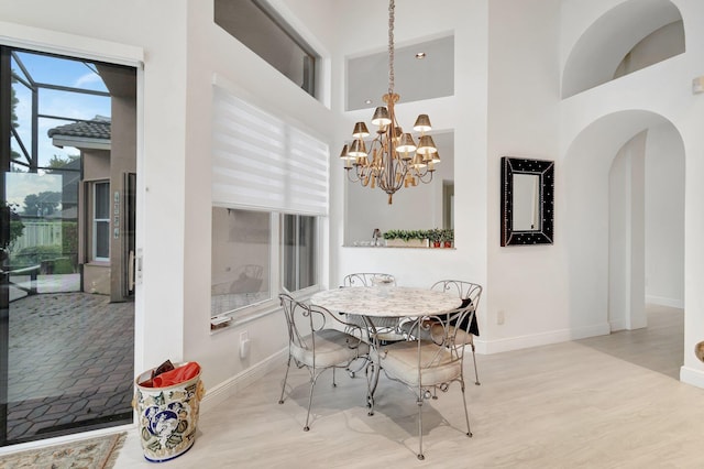 dining room with arched walkways, light wood-type flooring, a chandelier, and baseboards