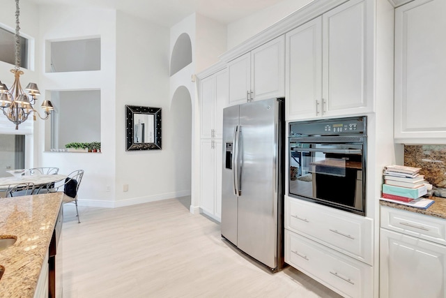 kitchen with arched walkways, light stone counters, oven, white cabinetry, and stainless steel refrigerator with ice dispenser