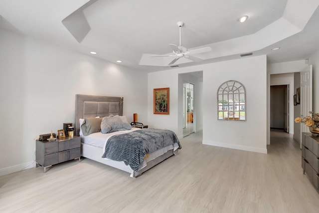bedroom with baseboards, a raised ceiling, visible vents, and light wood-style floors