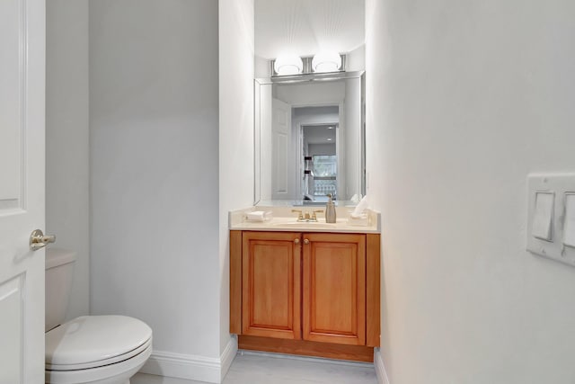 half bath with toilet, baseboards, and vanity