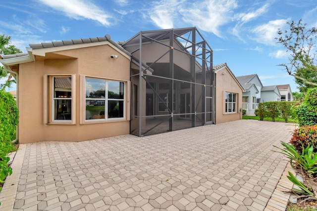 back of house with glass enclosure, a patio, and stucco siding