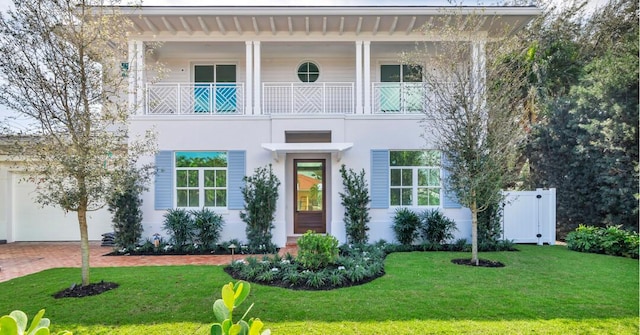 view of front facade with decorative driveway, a front yard, a balcony, and stucco siding