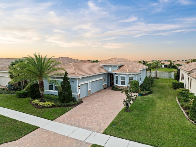 mediterranean / spanish-style home featuring a garage, a yard, decorative driveway, and a tiled roof