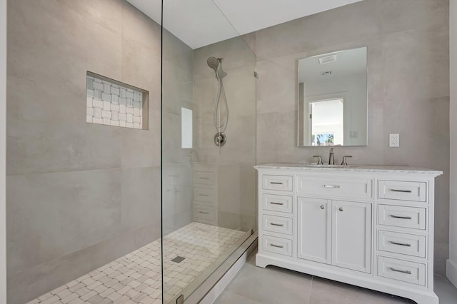 bathroom featuring tile patterned flooring, a walk in shower, tile walls, and vanity