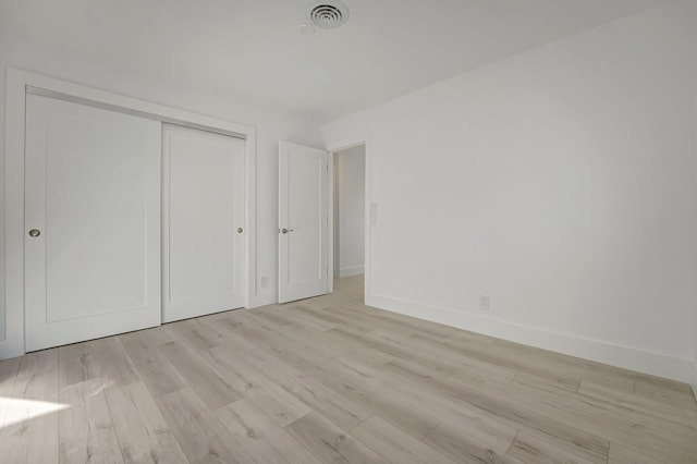 unfurnished bedroom featuring baseboards, light wood-style flooring, visible vents, and a closet