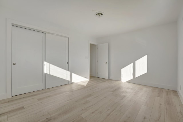 unfurnished bedroom featuring light wood finished floors, a closet, visible vents, and baseboards