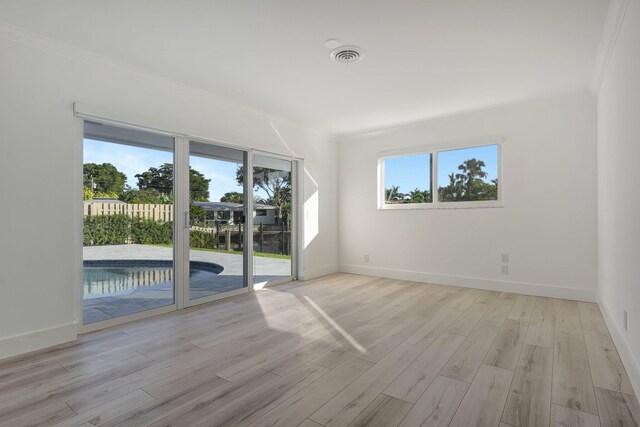 spare room featuring light wood-style floors, visible vents, ornamental molding, and baseboards