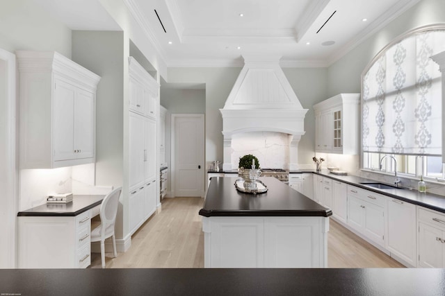 kitchen with dark countertops, custom range hood, white cabinetry, a kitchen island, and a sink