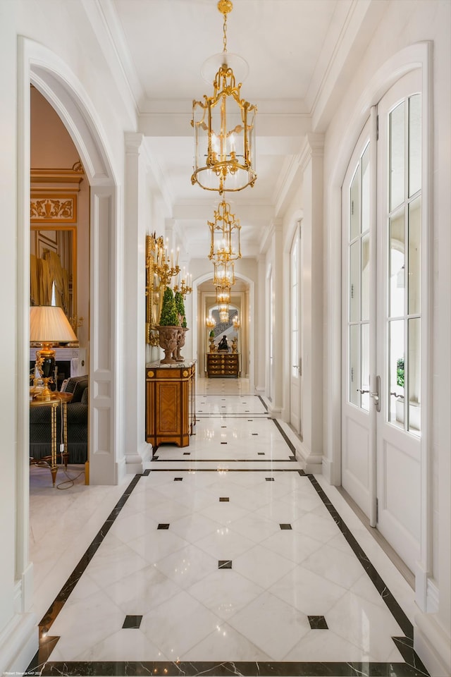 hall featuring arched walkways, crown molding, baseboards, and an inviting chandelier