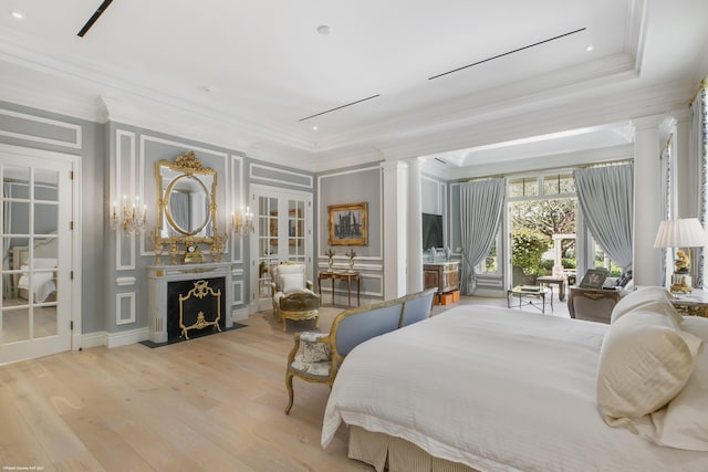 bedroom with crown molding, light wood-style floors, a fireplace with flush hearth, and ornate columns