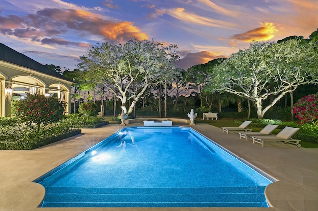 pool at dusk with a patio area and an outdoor pool