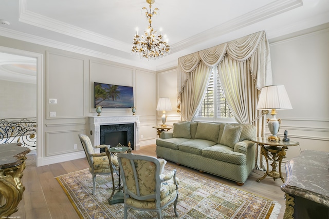 living room with ornamental molding, wood finished floors, an inviting chandelier, a fireplace, and a decorative wall