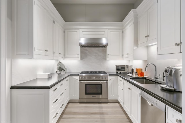 kitchen with white cabinets, dark countertops, appliances with stainless steel finishes, ventilation hood, and a sink