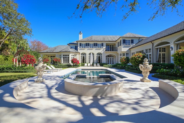 rear view of house featuring a balcony, a chimney, french doors, a patio area, and a pool with connected hot tub