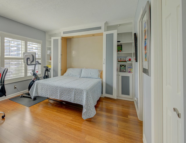 bedroom featuring light wood-type flooring, a textured ceiling, and baseboards