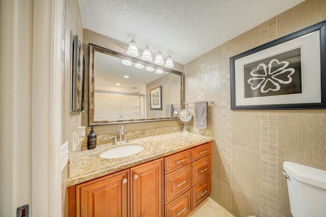 bathroom featuring tile walls, toilet, a shower with shower door, a textured ceiling, and vanity