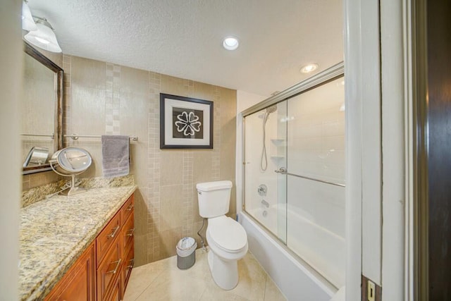 bathroom featuring a textured ceiling, tile patterned flooring, vanity, tile walls, and combined bath / shower with glass door