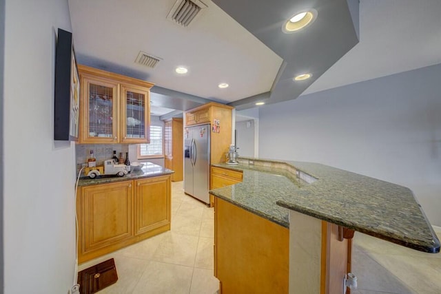 kitchen with a peninsula, visible vents, a kitchen breakfast bar, stainless steel fridge with ice dispenser, and glass insert cabinets