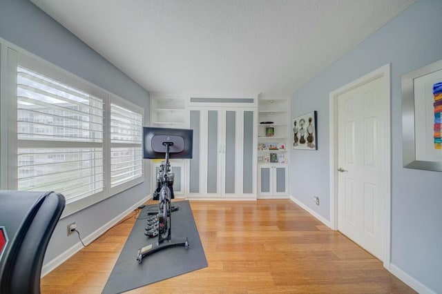 workout room featuring light wood-style floors, built in shelves, and baseboards