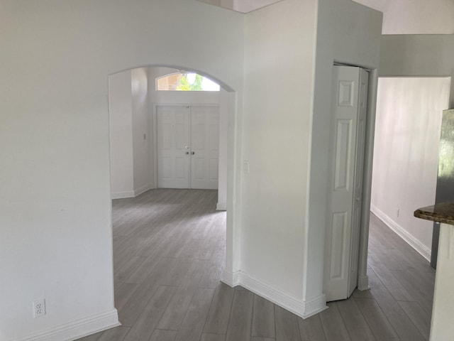 hall with arched walkways, baseboards, and wood finished floors