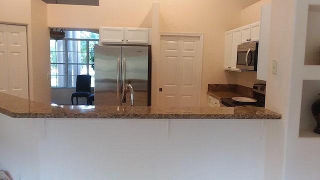 kitchen featuring a peninsula, white cabinetry, appliances with stainless steel finishes, and dark stone counters