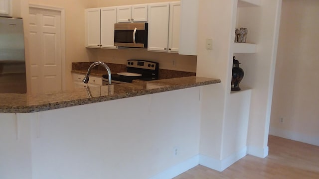 kitchen featuring stainless steel appliances, light wood-style floors, white cabinets, dark stone counters, and baseboards