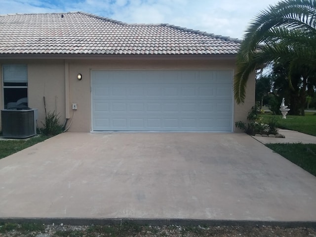 exterior space featuring a garage, driveway, a tiled roof, central AC, and stucco siding