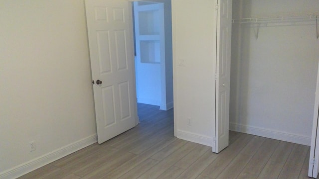 unfurnished bedroom with a closet, light wood-style flooring, and baseboards