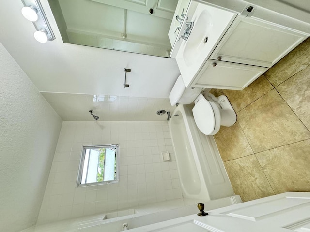 full bathroom with a textured wall, toilet, and tile patterned floors