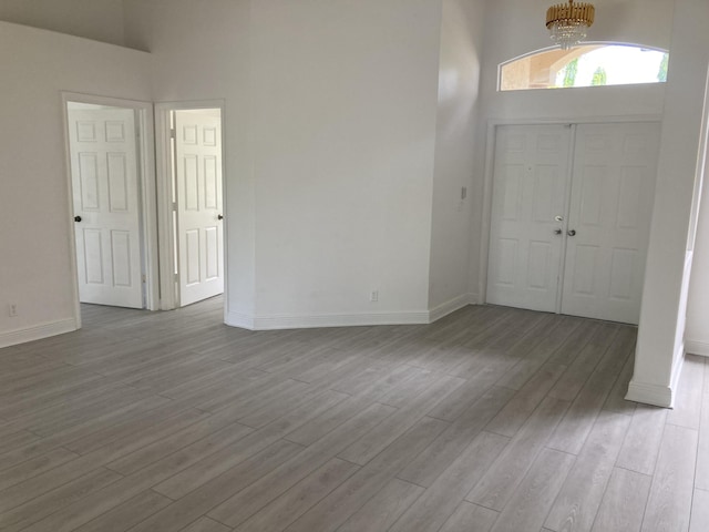 foyer featuring light wood-type flooring, a towering ceiling, baseboards, and a notable chandelier