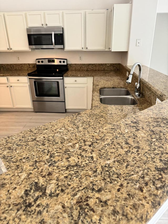 kitchen with appliances with stainless steel finishes, dark stone countertops, a sink, and white cabinets