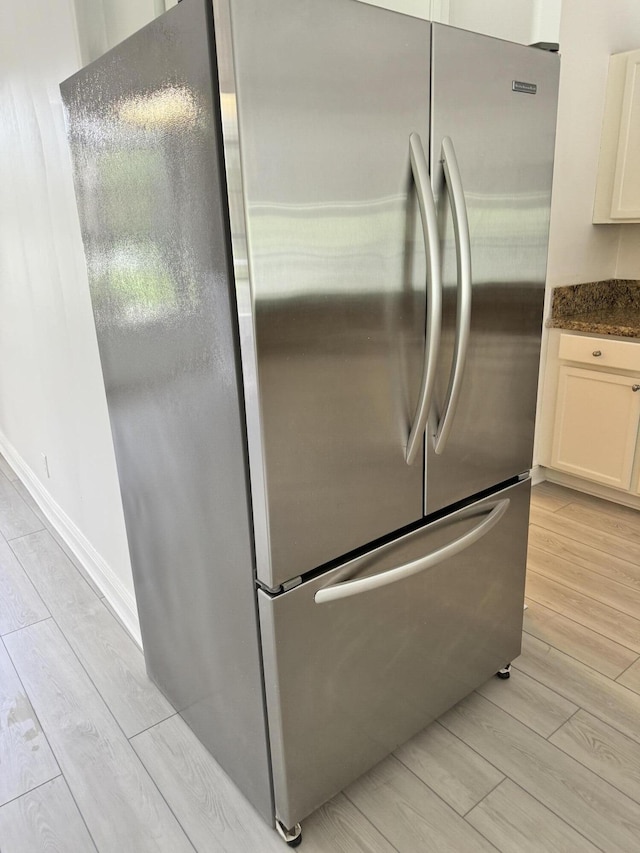 kitchen featuring baseboards, wood finish floors, freestanding refrigerator, and white cabinets