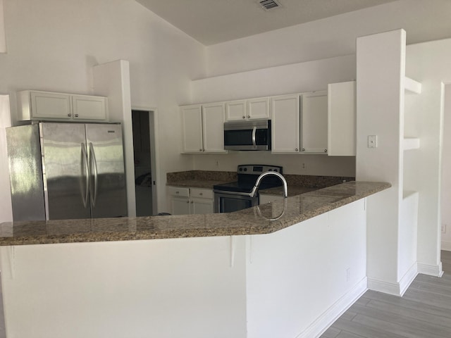 kitchen with stainless steel appliances, white cabinets, dark stone countertops, wood finished floors, and a peninsula