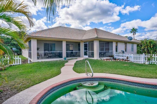 rear view of property with a lawn, a sunroom, a tiled roof, fence, and stucco siding