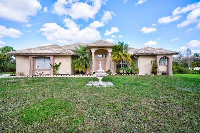 mediterranean / spanish home with a front yard, a tiled roof, and stucco siding