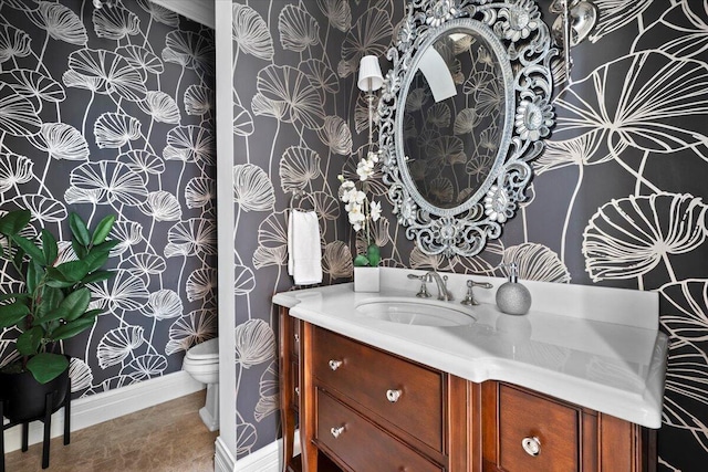 half bathroom featuring baseboards, vanity, toilet, and wallpapered walls