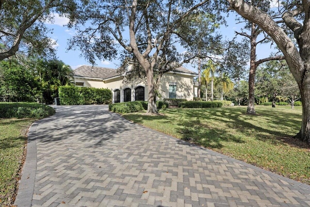 view of front facade featuring stucco siding, decorative driveway, and a front lawn