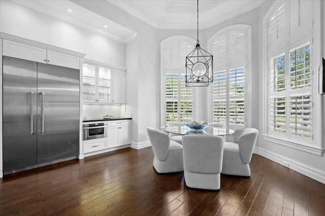 dining space featuring dark wood-style floors, crown molding, a notable chandelier, a high ceiling, and baseboards