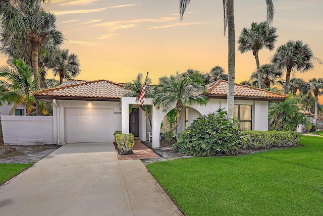 mediterranean / spanish house featuring a garage, a tile roof, driveway, a lawn, and stucco siding